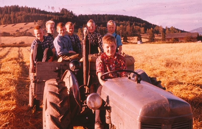 Sju gutter på en traktor og en henger med kornsekker på jordet på Haug, ca. 1963.